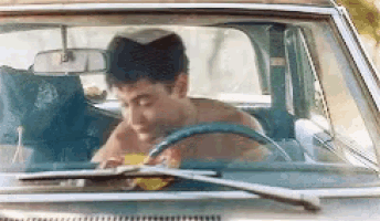 a shirtless man is driving a car with his eyes closed