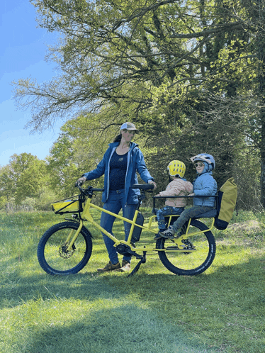 a woman is riding a yellow tandem bike with two children on the back