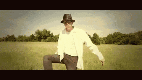 a man wearing a hat and sunglasses is kneeling in a field
