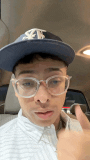 a man wearing a hat and glasses is giving a thumbs up sign