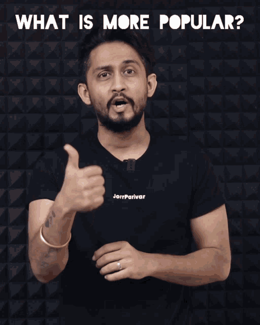 a man in a black t-shirt is pointing at something with the words " what is more popular " behind him