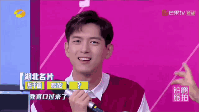 a man holding a microphone in front of a purple background with chinese writing
