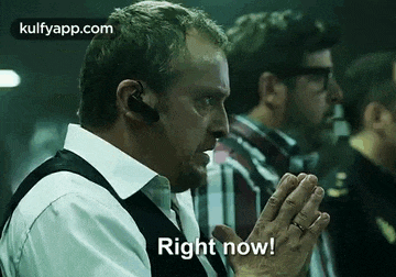 a man wearing a headset is sitting in a dark room with his hands folded and says `` right now ! ''