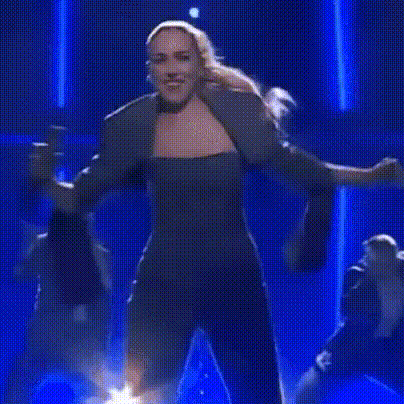 a woman in a suit is dancing on a stage with her arms outstretched in front of a crowd .