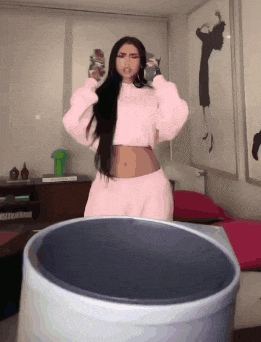 a woman in a pink outfit is standing next to a trash can