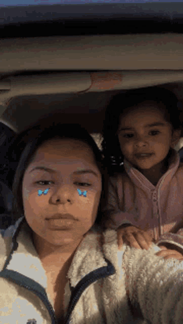 a woman and child are sitting in a car with tears on their faces .