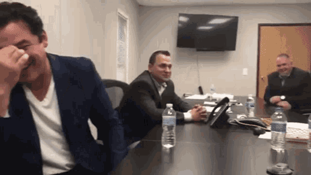 three men sit at a table with bottles of aquafina water on it