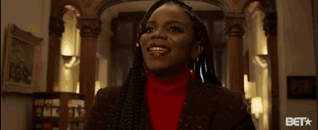 a woman with braids is standing in a hallway wearing a red sweater .