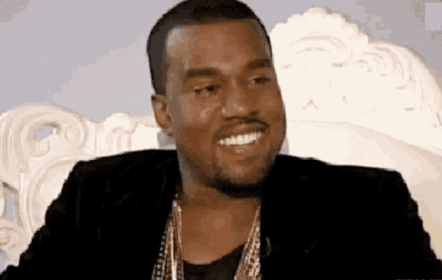 kanye west is smiling while sitting on a couch .