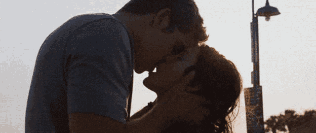 a man and a woman are kissing in front of a street lamp