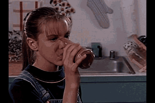 a young girl is drinking from a glass in front of a kitchen sink .