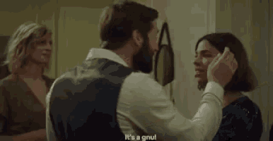 a man with a beard is touching a woman 's ear while a woman watches .
