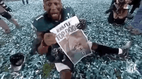 a football player is sitting on the ground holding a newspaper .