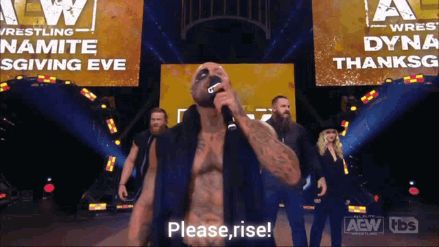a man speaking into a microphone in front of a sign that says aew