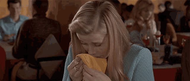 a woman in a blue jacket wipes her nose with a yellow napkin
