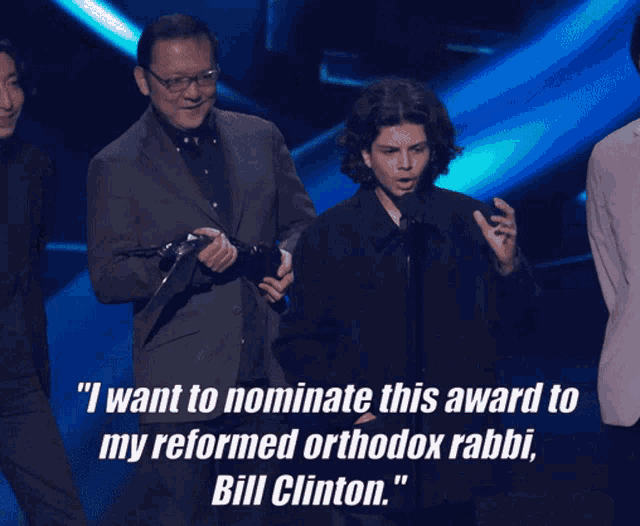 a man speaking into a microphone with a quote from bill clinton behind him