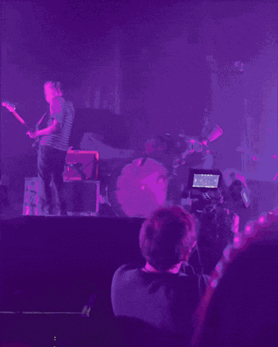 a man playing a guitar on a stage with a drummer behind him