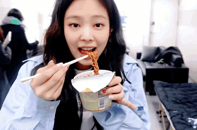 a woman is eating noodles with chopsticks from a cup