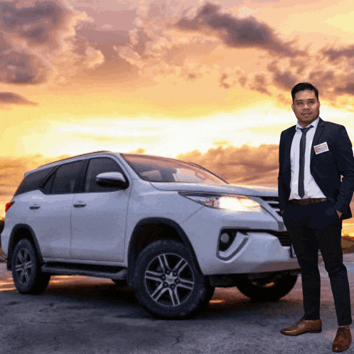 a man in a suit and tie stands in front of a car