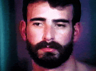 a man with a beard looks at the camera with a purple background