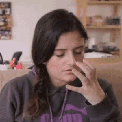 a woman is sitting on a couch holding her nose because she is smelling something .