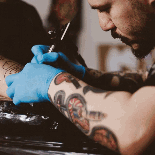 a man with blue gloves is getting a tattoo on someone 's arm
