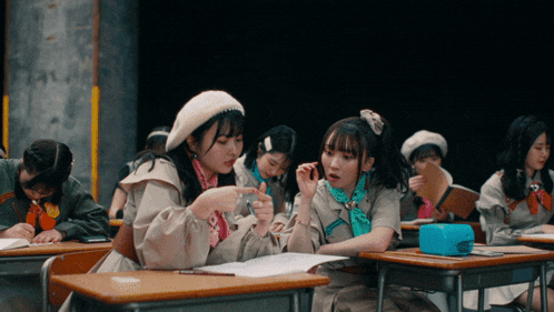 a group of girls are sitting at desks in a classroom and one girl is pointing at something