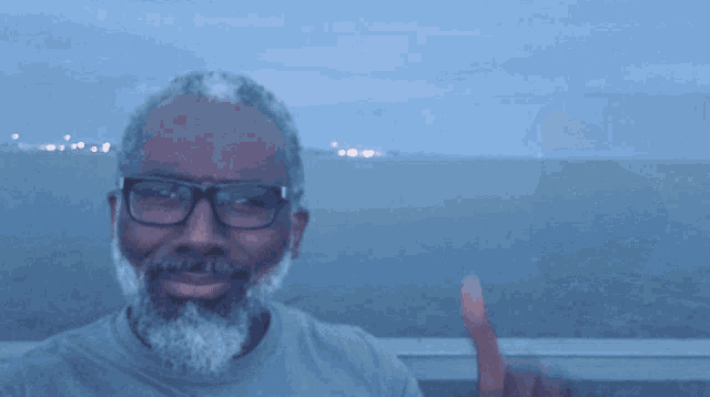 a man wearing glasses and a beard holds up his fist in front of the ocean
