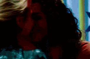 a woman with curly hair is being kissed by another woman