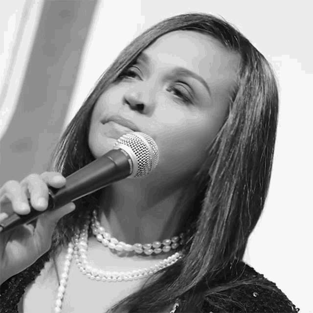 a woman singing into a shure microphone while wearing pearls