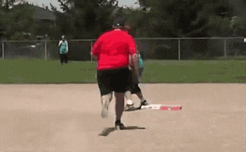 a man in a red shirt is running on a baseball field while a woman watches .