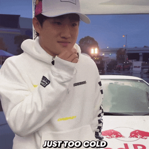a man wearing a white hoodie and a baseball cap is standing in front of a car that says just too cold