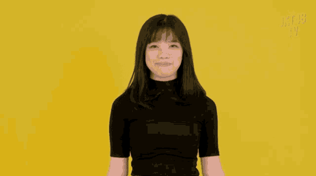 a young woman wearing a black shirt is standing in front of a yellow background .