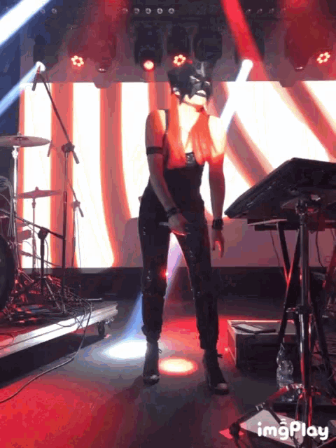 a woman in a mask stands on a stage in front of a keyboard with the word imgplay on the bottom