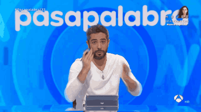 a man laughs in front of a blue background with the word pasapalabra on it