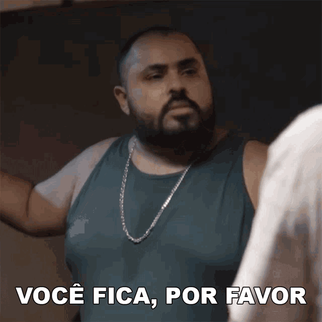 a man with a beard is wearing a green tank top and a silver chain around his neck and says " você fica por favor "