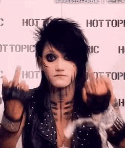 a man with black hair is giving the middle finger in front of a wall that says hot topic