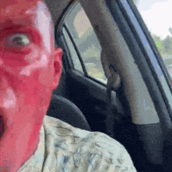 a man with a red face is sitting in a car