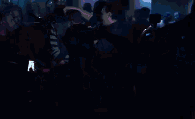 a crowd of people are gathered in a dark room and a man is taking a picture with his phone