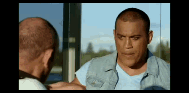 a man in a denim vest is looking at his reflection in a mirror