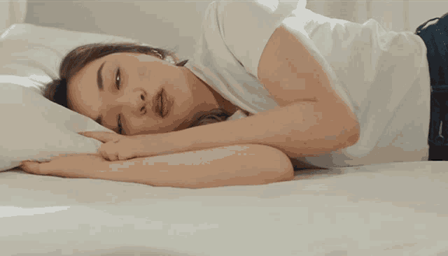 a woman in a white shirt is laying on a white bed