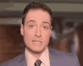 the man is wearing a suit and tie and making a funny face .