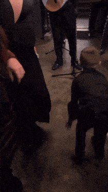 a young boy in a black suit is dancing in front of a guitar player