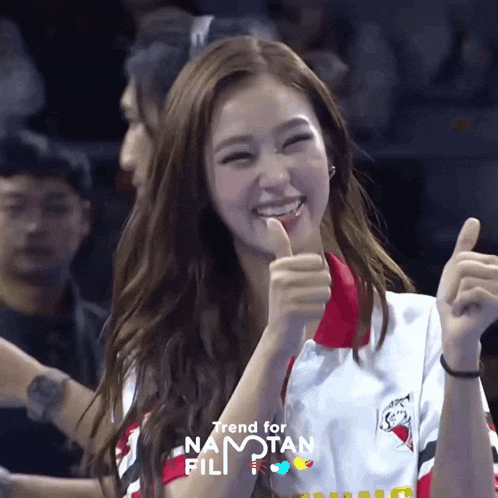 a woman is smiling and giving a thumbs up in front of a trend for namotan fili logo