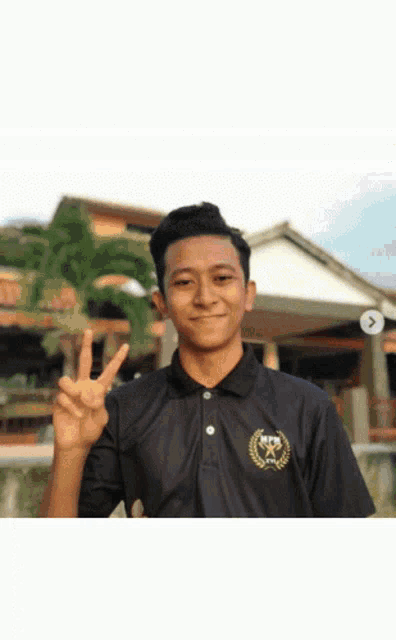 a man wearing a black shirt with a gold emblem on it giving the peace sign