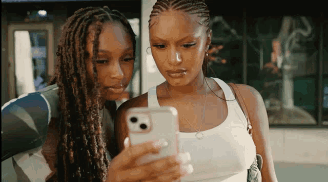 two women are looking at a cell phone together and one has dreadlocks