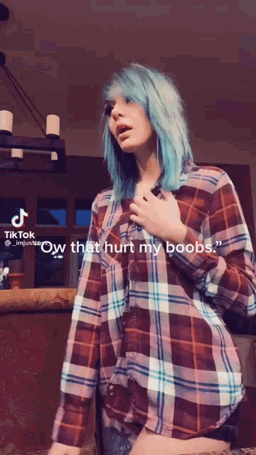 a woman with blue hair is wearing a plaid shirt that says " ow that hurt my boobs " on the bottom