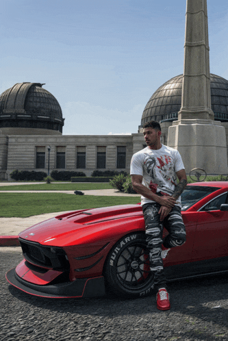 a man leans against a red car that has the word rrw on the wheels