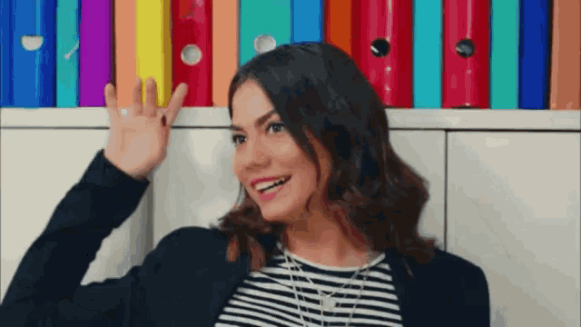 a woman in a striped shirt is waving in front of a row of colorful folders