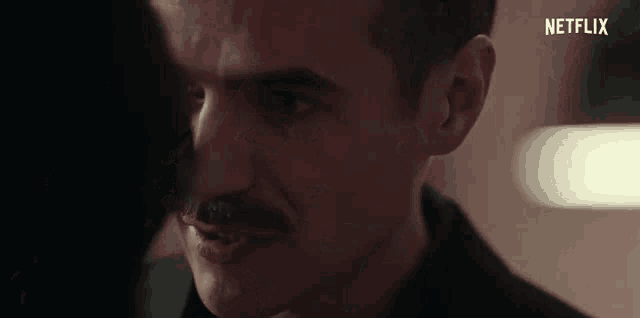 a close up of a man 's face with a mustache and a woman 's face in the background .
